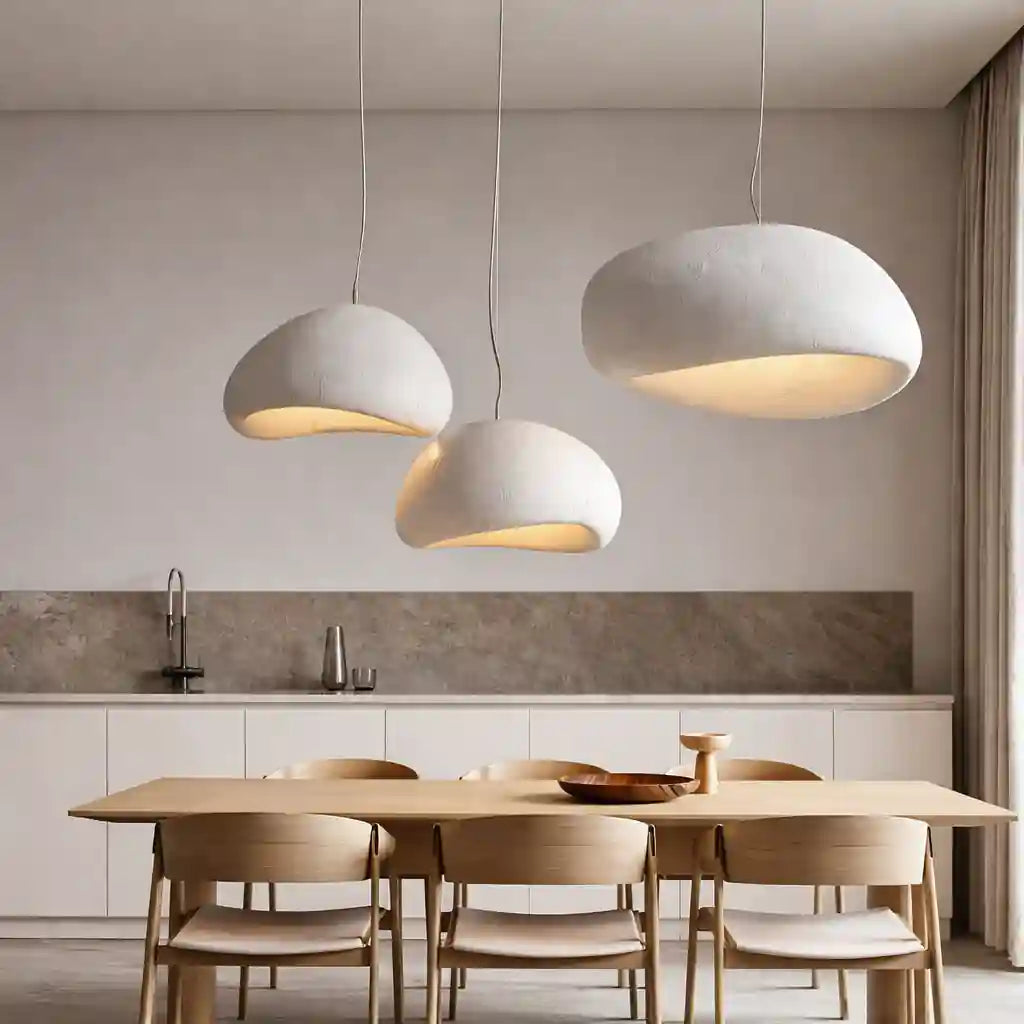 Three white cement pendant lights with rounded, organic shapes hanging over a light wood dining table in a modern kitchen.