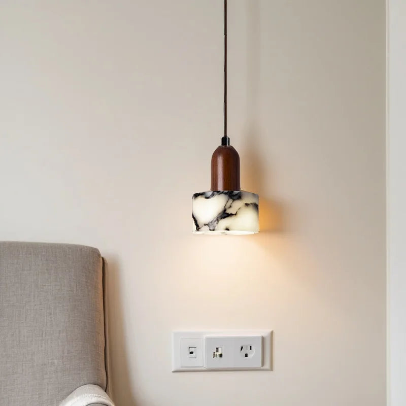 Modern pendant light with marble-effect shade and wooden top above upholstered bed headboard.