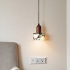 Modern pendant light with marble-effect shade and wooden top above upholstered bed headboard.