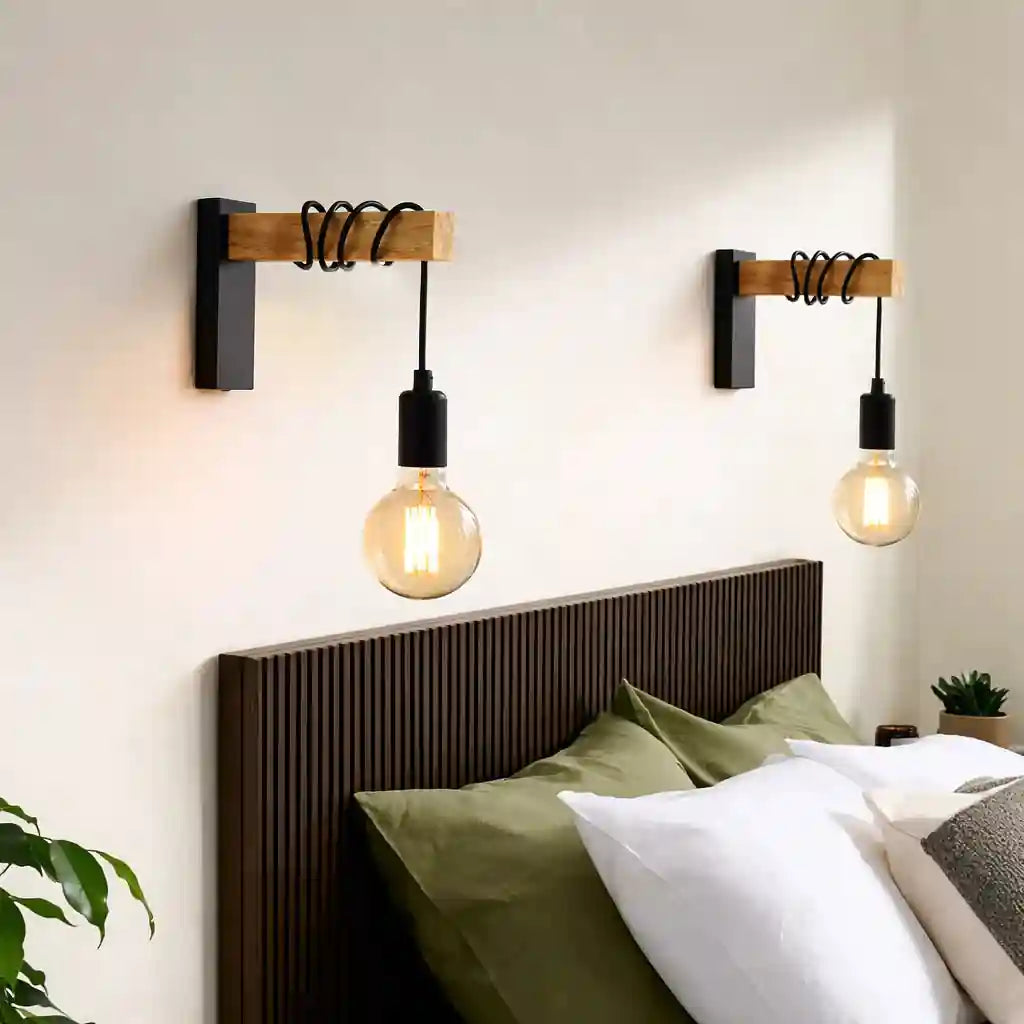 Pair of black industrial wall lamps with wooden mounts and exposed LED bulbs above a bed with green and white pillows.